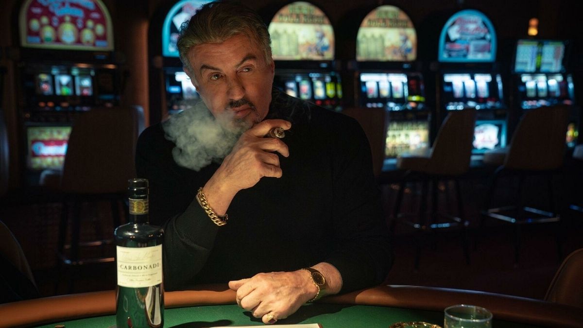 Mobster Dwight Manfredi (Sylvester Stallone) smoking a cigar and looking pensive in his casino in Tulsa King Season 2