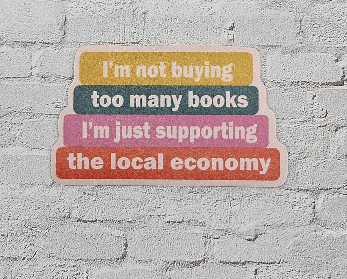 Image d'un autocollant en vinyle conçu pour ressembler à une pile de livres qui dit "Je n'achète pas trop de livres, je soutiens juste l'économie locale"