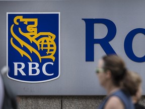 Des piétons sont photographiés ici marchant devant un panneau de la Banque Royale du Canada.