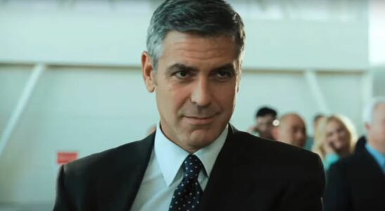 George Clooney wears a sly smile while standing in the airport in Up In The Air.