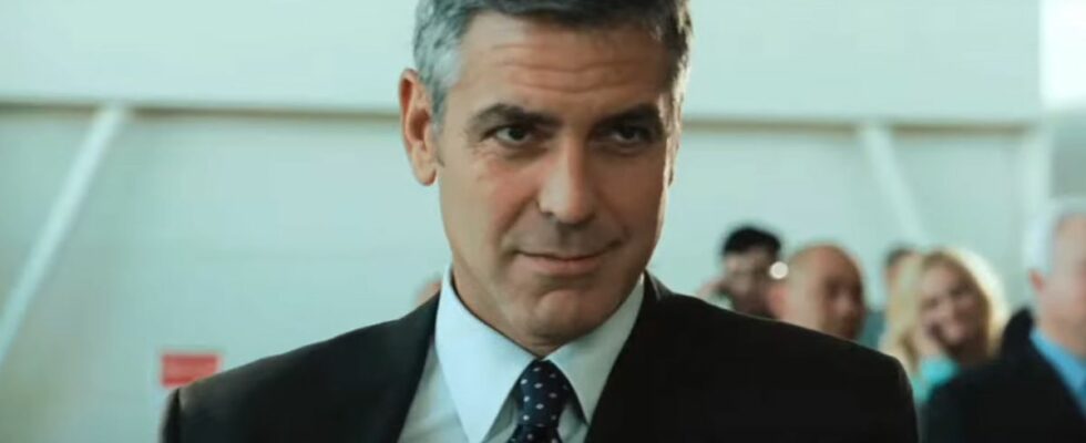 George Clooney wears a sly smile while standing in the airport in Up In The Air.