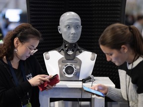 Les gens vérifient leurs téléphones pendant qu'AMECA, un robot IA, regarde la conférence sur l'intelligence artificielle All In à Montréal, au Québec, en 2023.