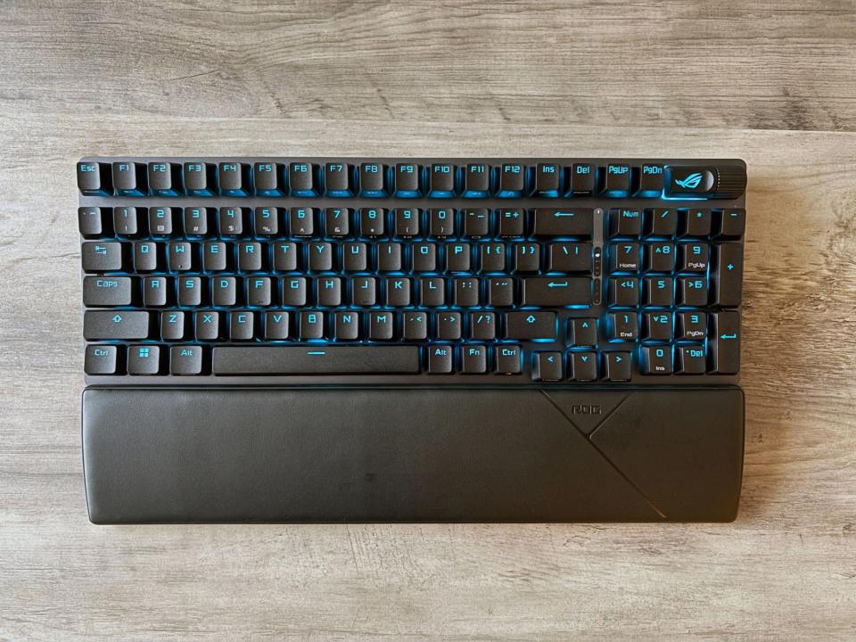 Le clavier de jeu sans fil ASUS ROG Strix Scope II 96 repose sur une table en bois marron clair.