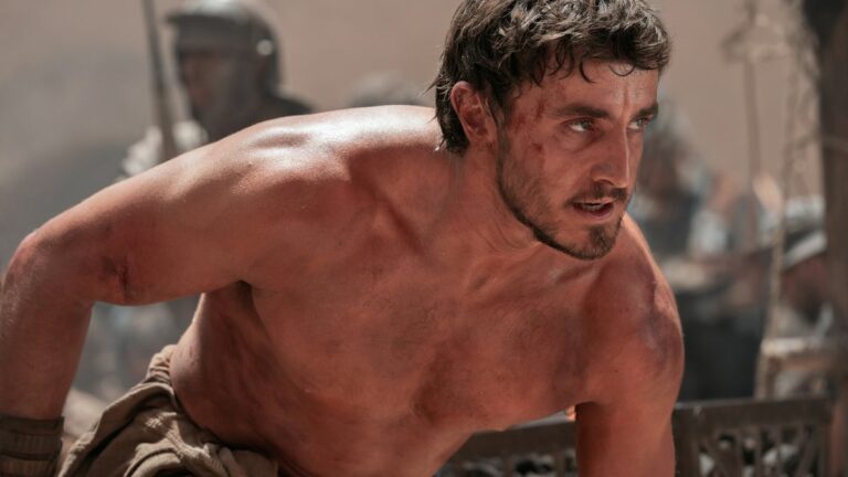 A bare chested Paul Mescal crouches in the middle of a battle in Gladiator II.