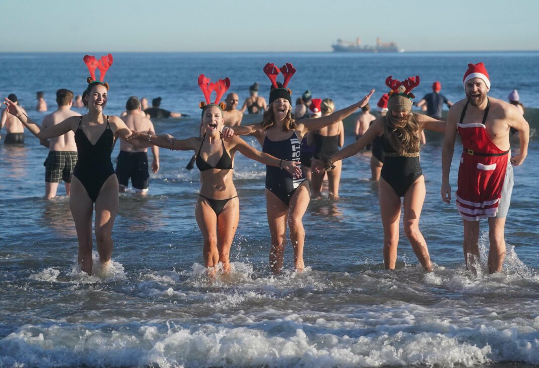 Nageurs intrépides se dirigent vers la plage pour une baignade festive le jour de la boxe, arborant chapeaux de Noël et bois de cerf.